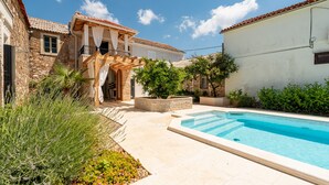 A pool area with a stone building, a wooden staircase, and a white wall.