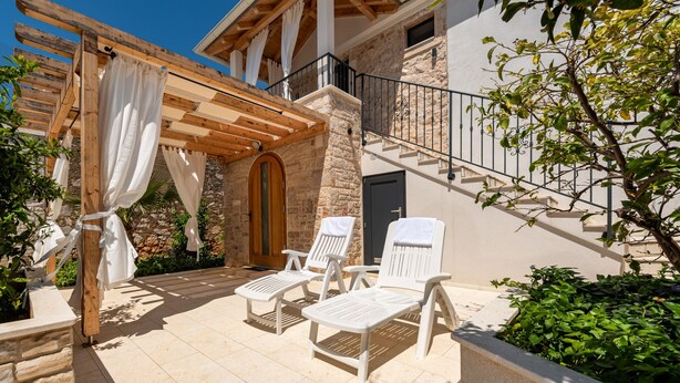 A covered outdoor seating area with stone walls and a wooden pergola.