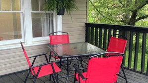 A covered porch with a table and four red chairs, a hanging plant, and a view of greenery. - Hillside Hideaway (Weber City)