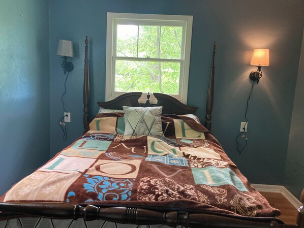 Un dormitorio con cama, ventana y dos lámparas fijadas a la pared.
