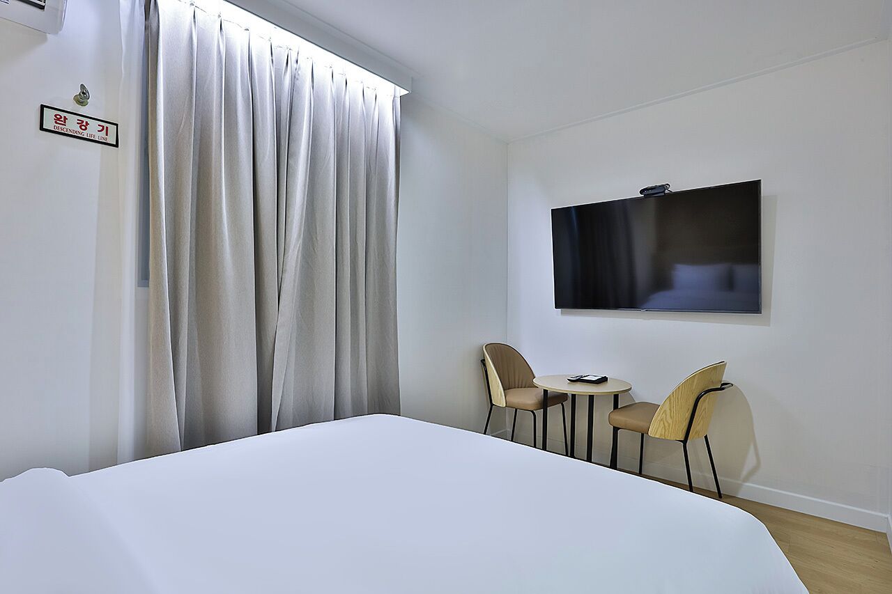 Ein Hotelzimmer mit Bett, zwei Stühlen, einem kleinen Tisch, einem Fernseher und einem Schild an der Wand.