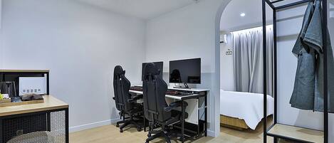 A modern hotel room with a desk, two monitors, a chair, a bed, and a clothing rack.