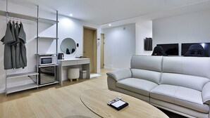 A modern living room with a white sofa, a coffee table, a TV, and a desk with a computer and a microwave. - Brown Dot Hotel Gumi Okgye Branch (Gumi)