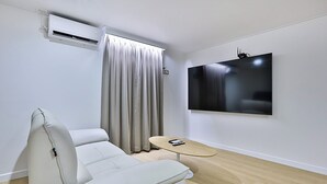 A modern living room with a white sofa, a small round table, a mounted TV, and an air conditioning unit. - Brown Dot Hotel Gumi Okgye Branch (Gumi)