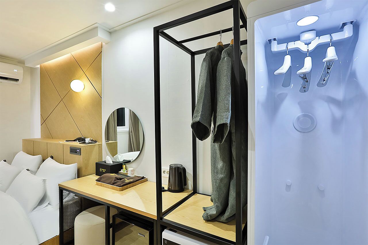 A hotel room with a bed, a desk with a coffee maker, a mirror, a wardrobe, and a shoe display.