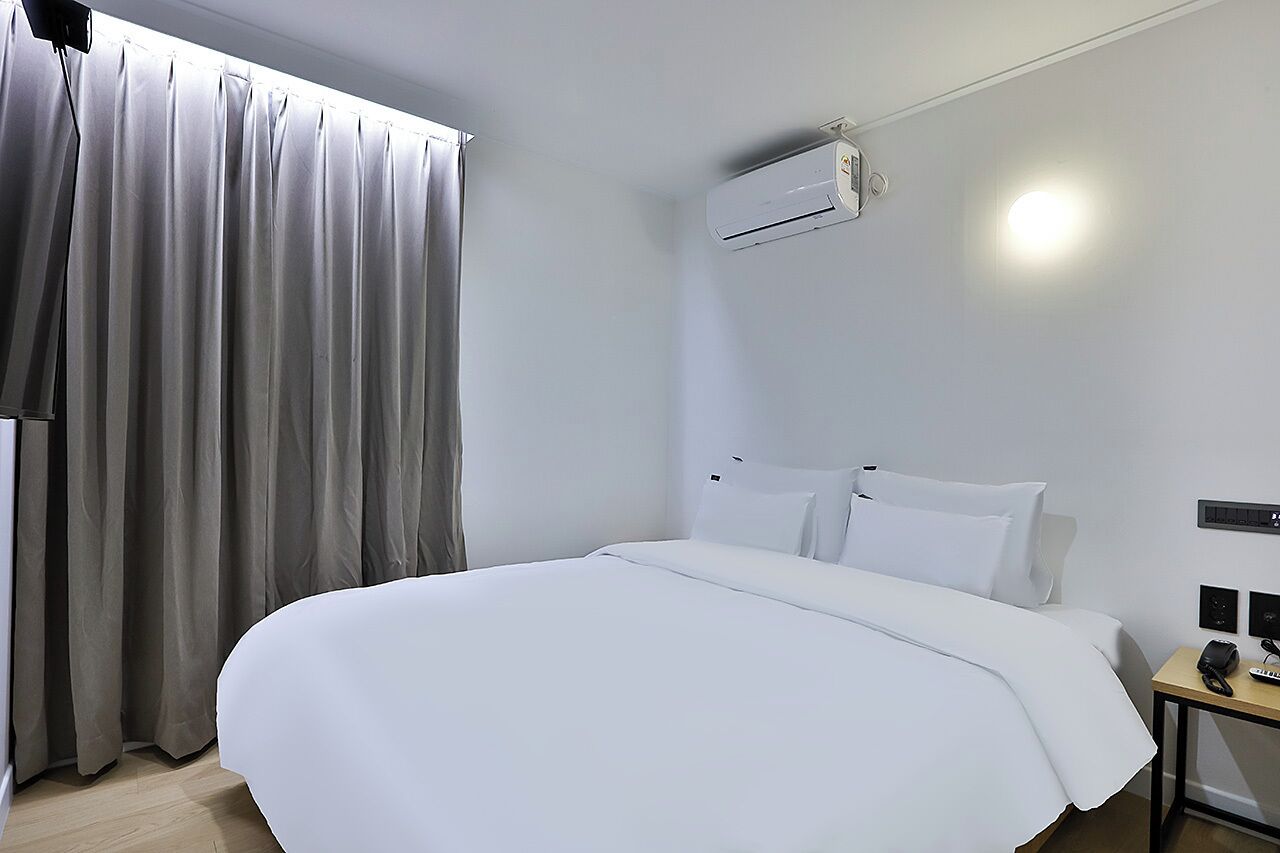 Ein Hotelzimmer mit einem Bett, einem Nachttisch mit Telefon und einer Klimaanlage an der Wand.