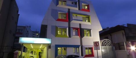 Un edificio de hotel con diseño moderno, varios pisos y un automóvil estacionado al frente.