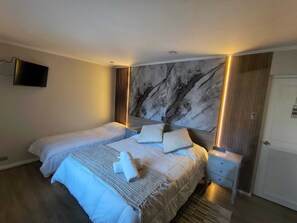 A bedroom with two beds, a TV mounted on the wall, a marble headboard, and a wooden wardrobe. - Hotel Agora (Viña del Mar)