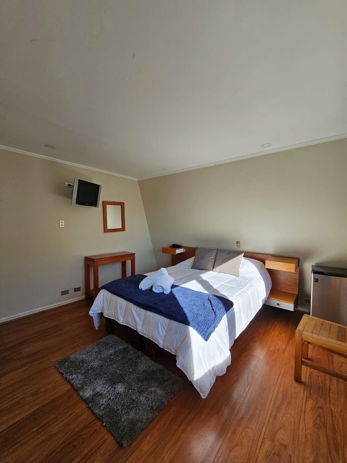 A bedroom with a bed, bedside tables, a TV, and a small desk.