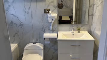 Un baño con inodoro, lavabo, espejo y secador de pelo fijado en la pared.