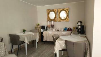 Un comedor con mesas, sillas, una cafetera y un espejo decorativo.