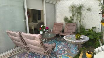 Een terras met een mozaïek vloer, twee comfortabele stoelen, een kleine tafel met een potplant, en een glazen schuifdeur naar een binnenruimte.