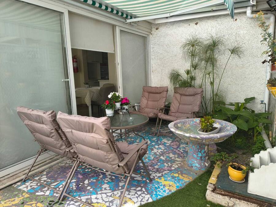 Een terras met een mozaïek vloer, twee comfortabele stoelen, een kleine tafel met een potplant, en een glazen schuifdeur naar een binnenruimte.