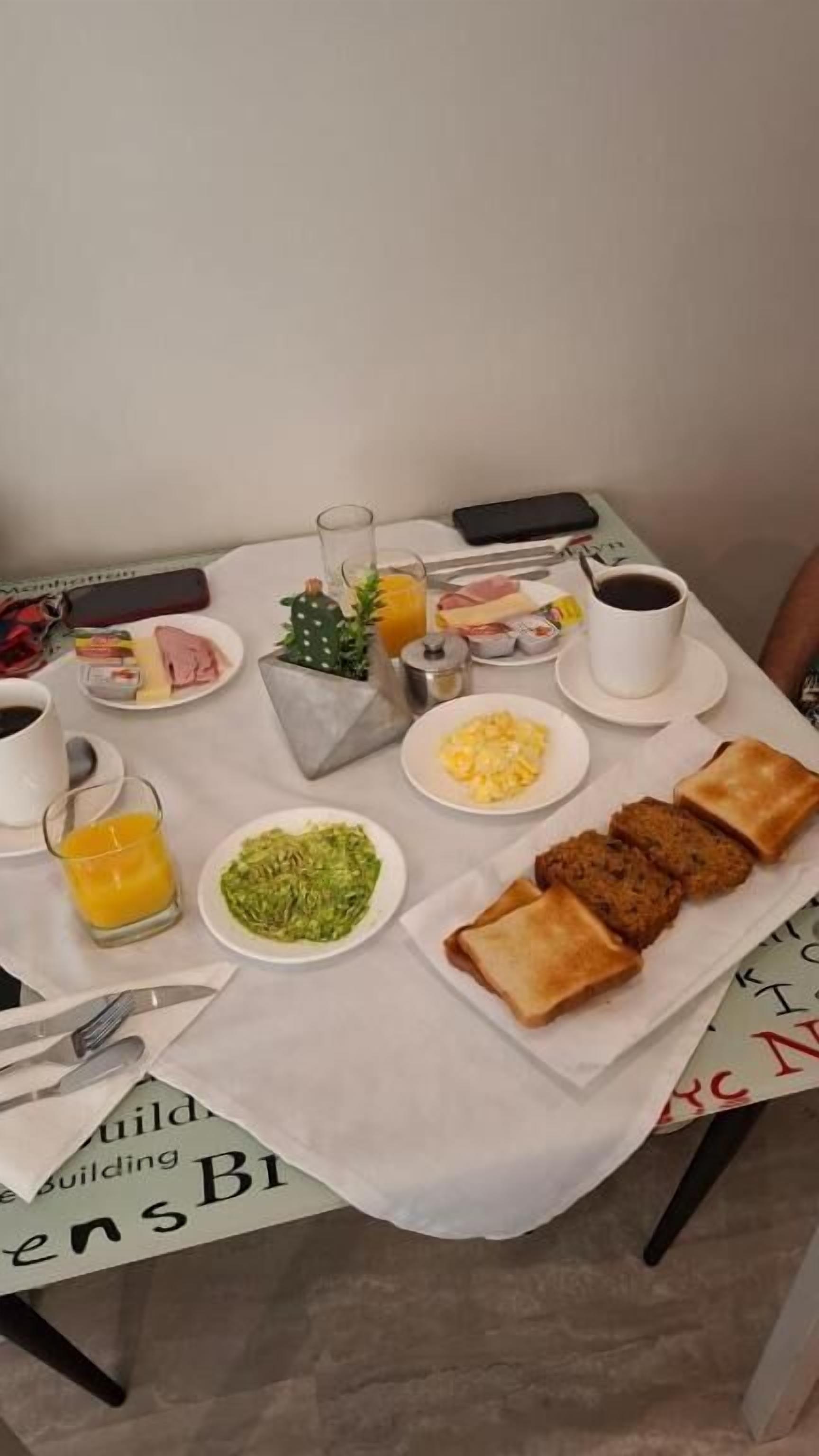 A breakfast table with plates of food, a glass of orange juice, a cup of coffee, and a mobile phone.