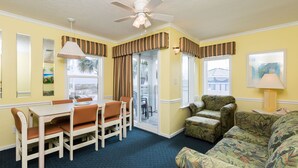 A room with a dining table, chairs, a patterned sofa, a ceiling fan, and a window with curtains. - 2-BR Beachfront Condo with Balcony Views! (North Myrtle Beach)