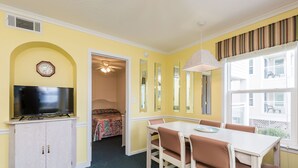 A dining area with a table and chairs, a television on a cabinet, and a hallway leading to a bedroom. - 2-BR Beachfront Condo with Balcony Views! (North Myrtle Beach)