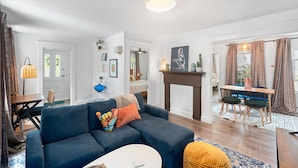 A living room with a blue sofa, a dining table with chairs, a fireplace, and a large window with curtains. - Charming 2-bedroom apartment near Providence (West Warwick)
