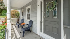 A porch with two Adirondack chairs and a small table, a gray door with a wreath, and a white railing. - Charming 2-bedroom apartment near Providence (West Warwick)