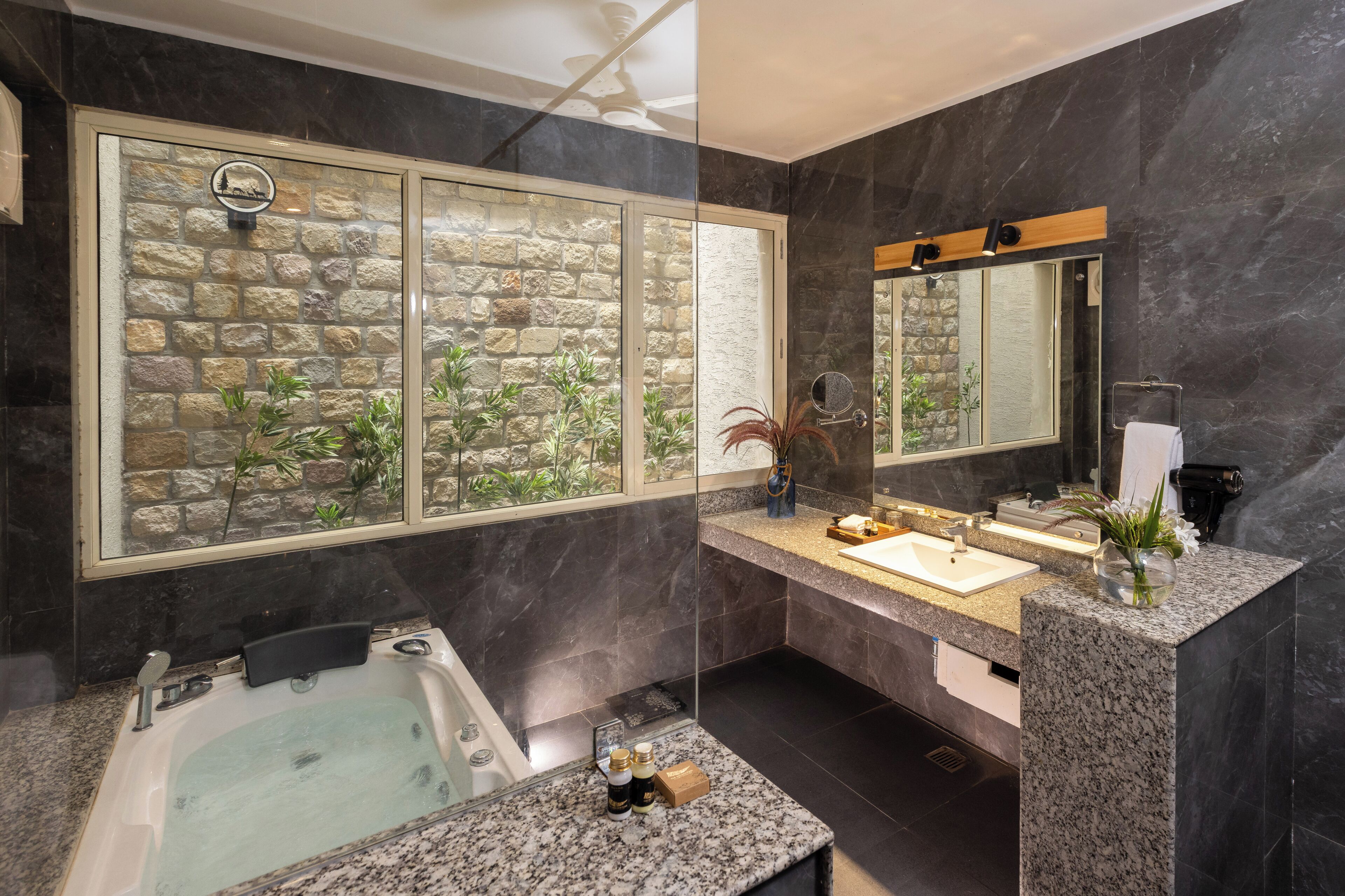 A modern bathroom with a stone wall, a large window, a bathtub, and a vanity with a mirror.