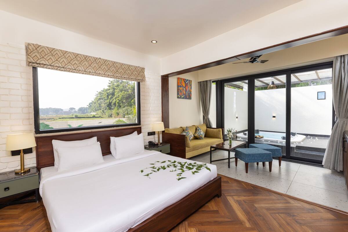 A hotel room with a large bed, a sofa, a coffee table, and a sliding glass door leading to a balcony.