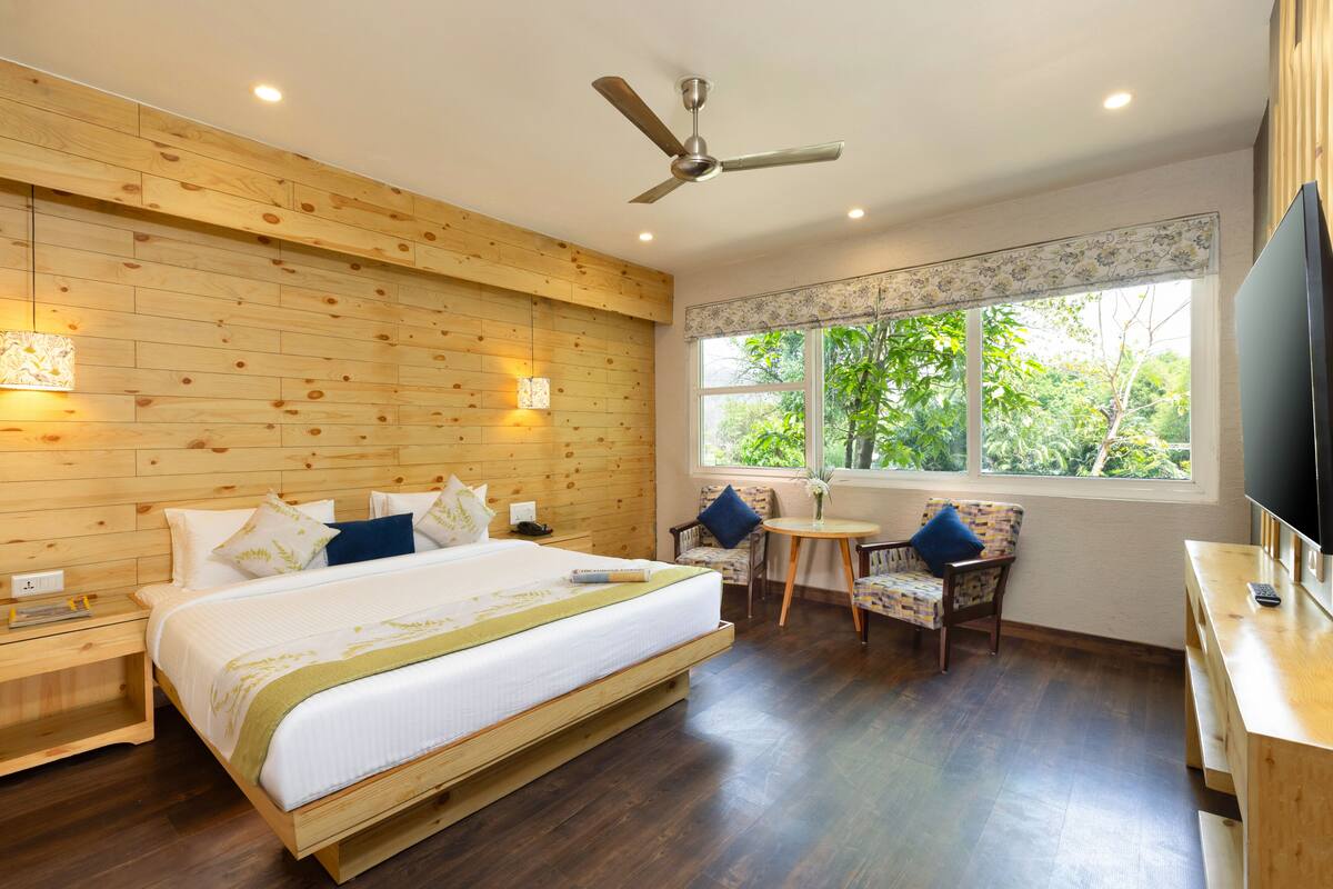 A bedroom with a bed, a ceiling fan, a small table, a chair, and a TV.