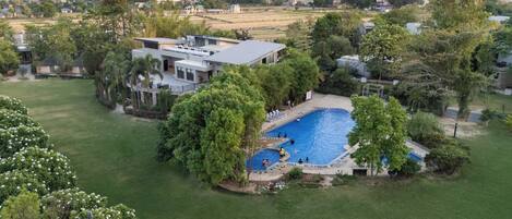 A residential property with a swimming pool, a large lawn, and a view of the surrounding area.