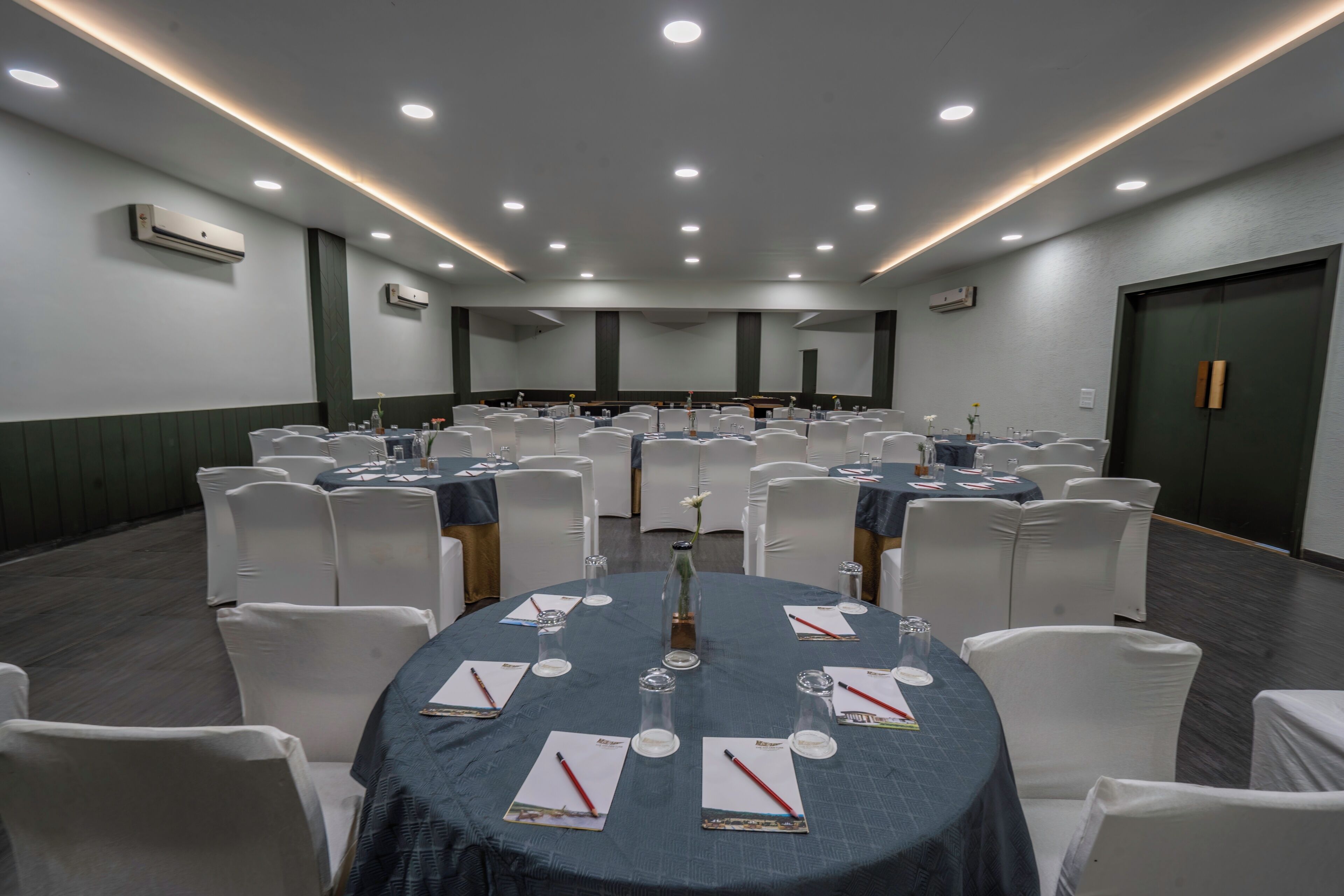 A conference room with round tables, white chairs, and a dark tablecloth.