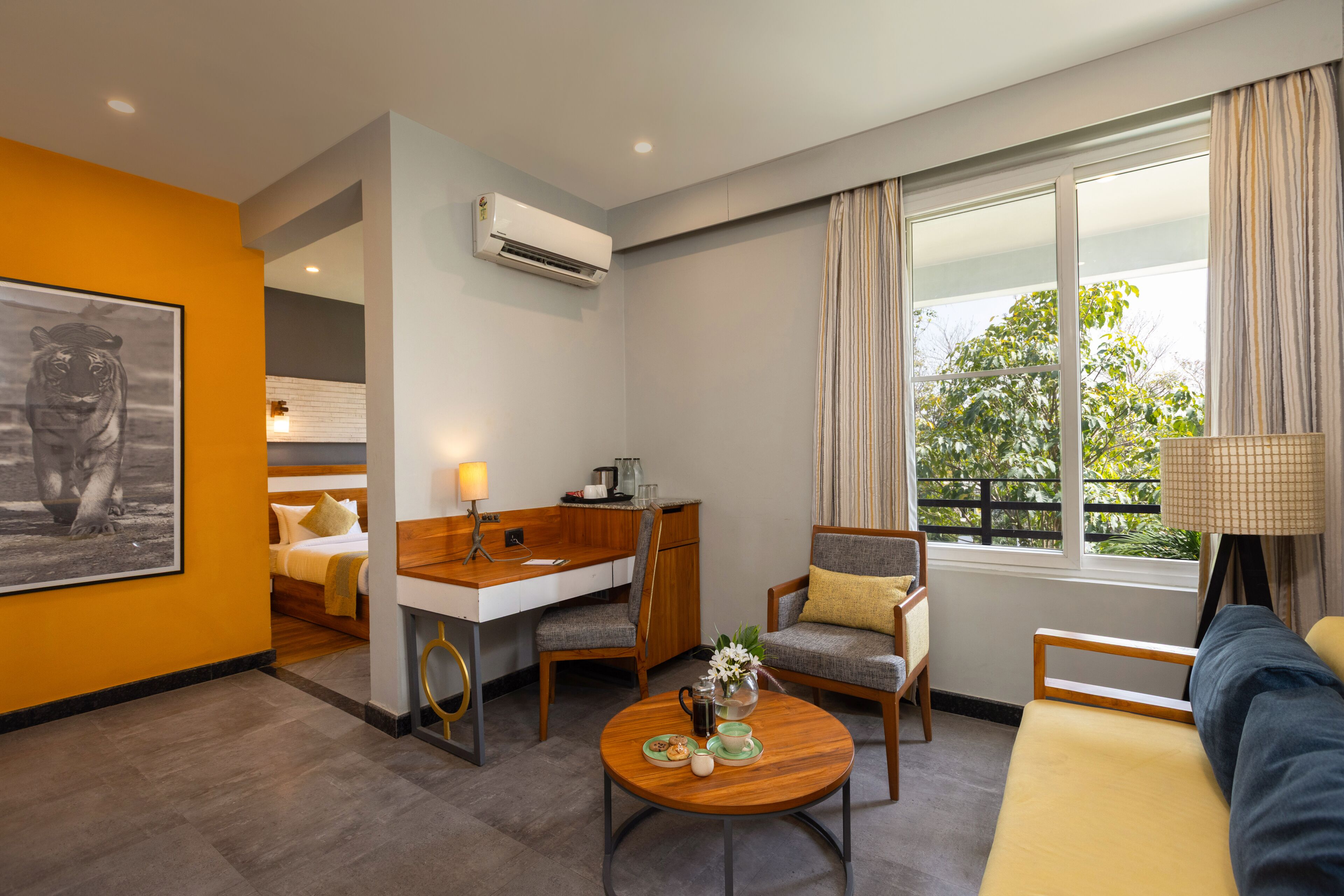 A hotel room with a bed, a desk, a chair, a sofa, a coffee table, and a window with curtains.