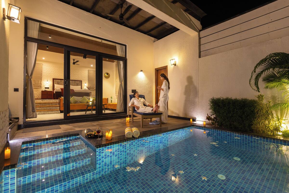 A swimming pool with a glass bottom, a person relaxing by the pool, and a room with a bed and a window.