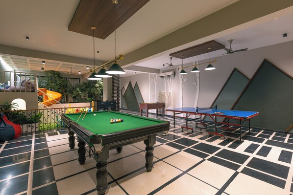 Une table de billard avec des billes, une table de ping-pong et un canapé vert.
