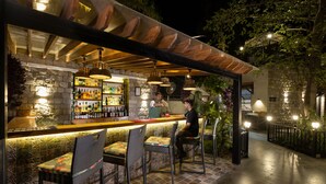 Een buitengebied met een bar, rieten stoelen, een stenen muur en een houten pergola.