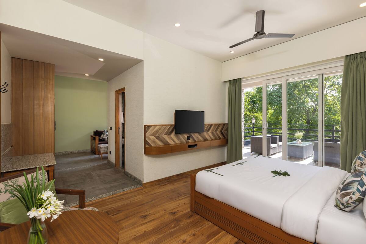 A hotel room with a bed, a TV mounted on the wall, a ceiling fan, and a view of the outdoors.