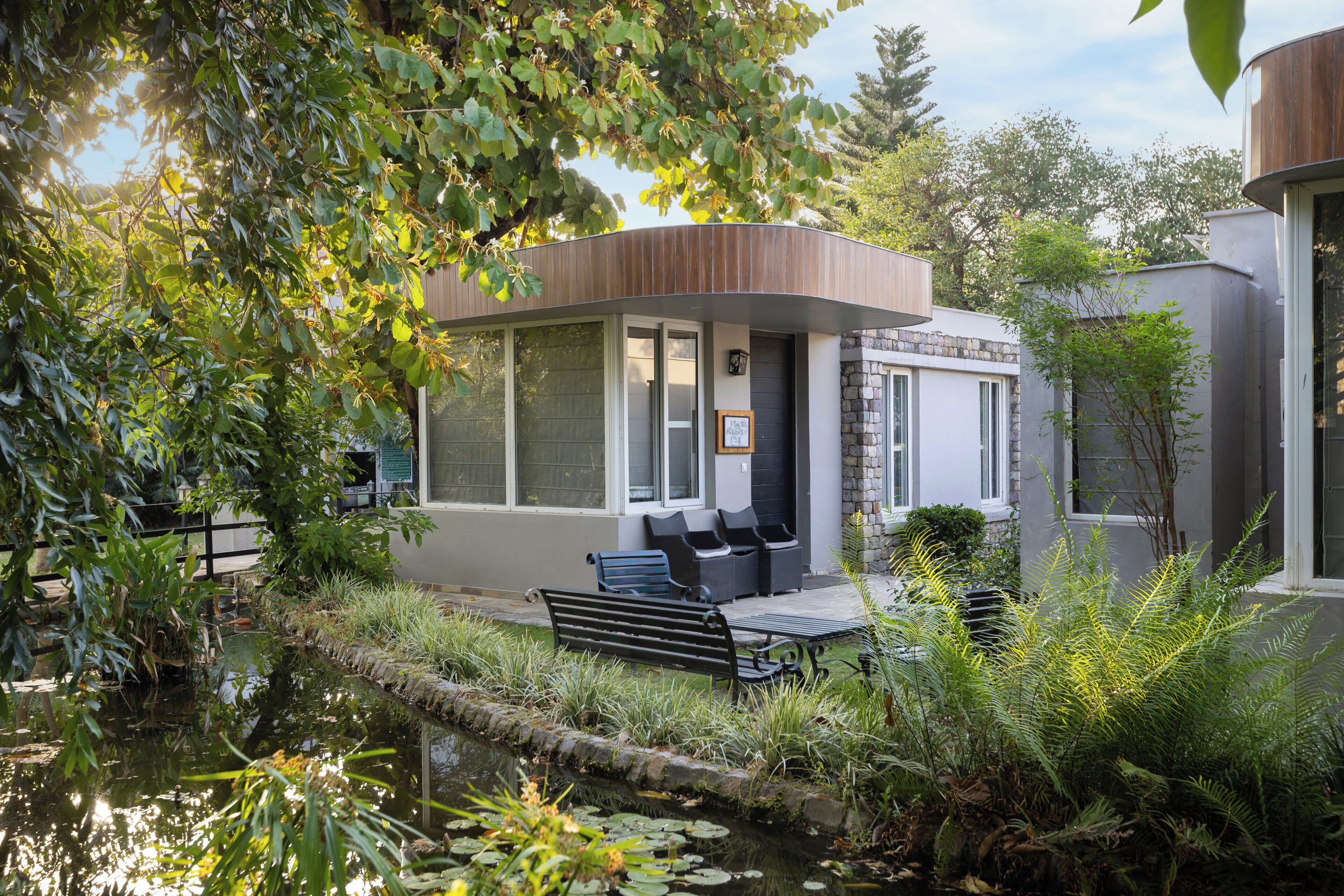 A modern building with a curved roof, a seating area with benches, and a small pond with water lilies.