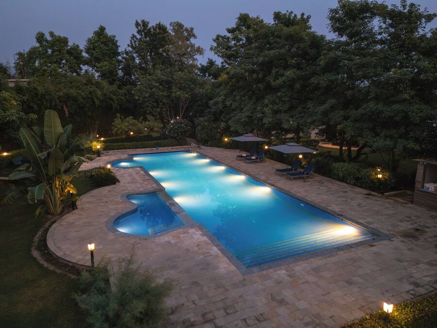 Una piscina rectangular con un jacuzzi pequeño, rodeada por un solárium empedrado y abundante vegetación.