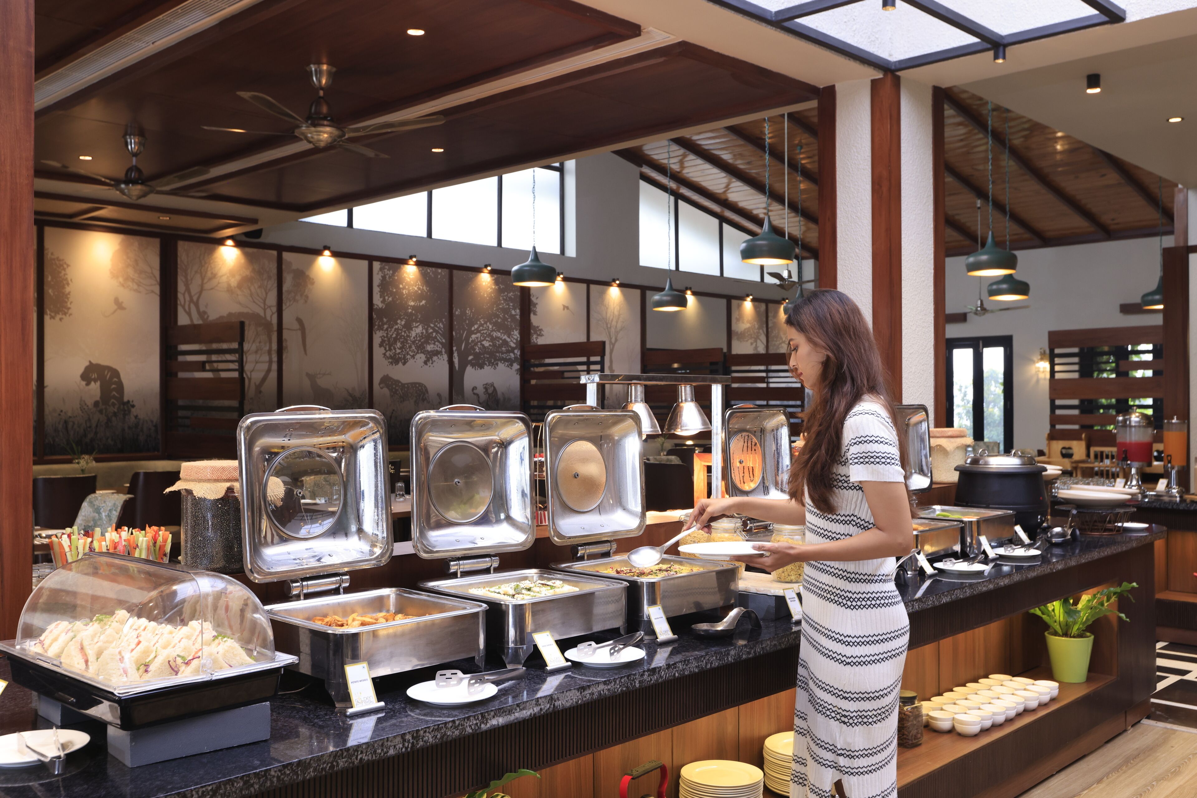 A buffet area with multiple food dispensers, a counter with a server, and a large window with natural light.