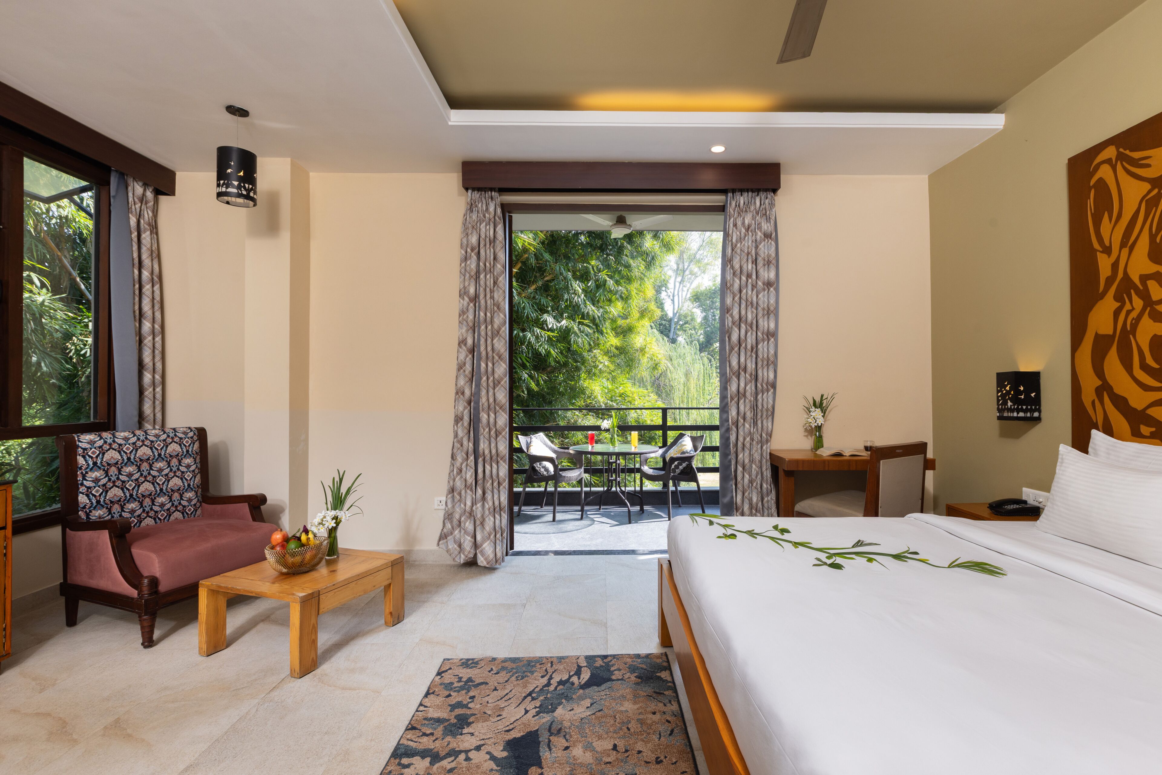 Une chambre d’hôtel avec un lit, une chaise, une petite table et un balcon donnant sur la verdure.