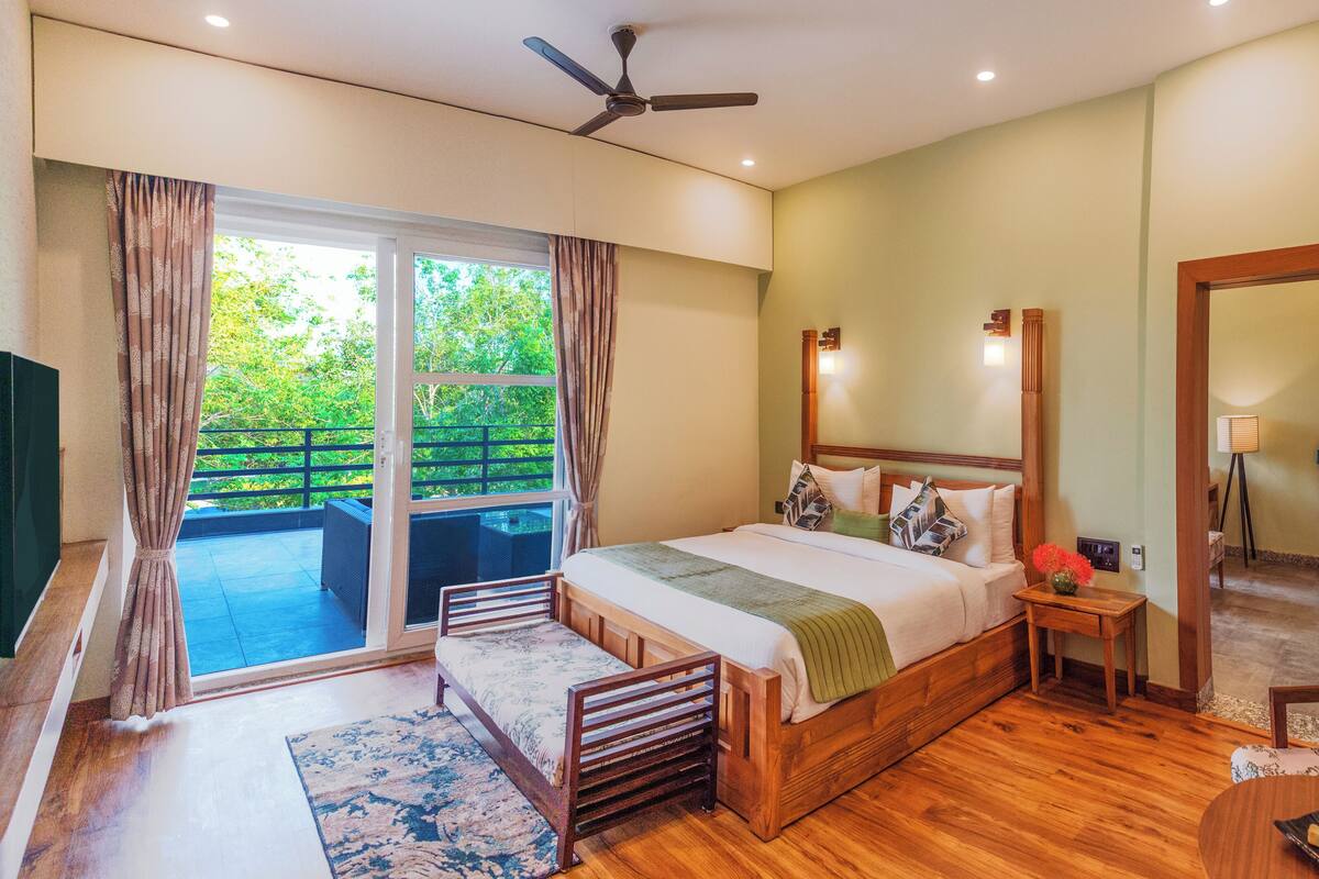 A bedroom with a bed, a nightstand, a chair, a table with cookies, a mirror, and a ceiling fan.