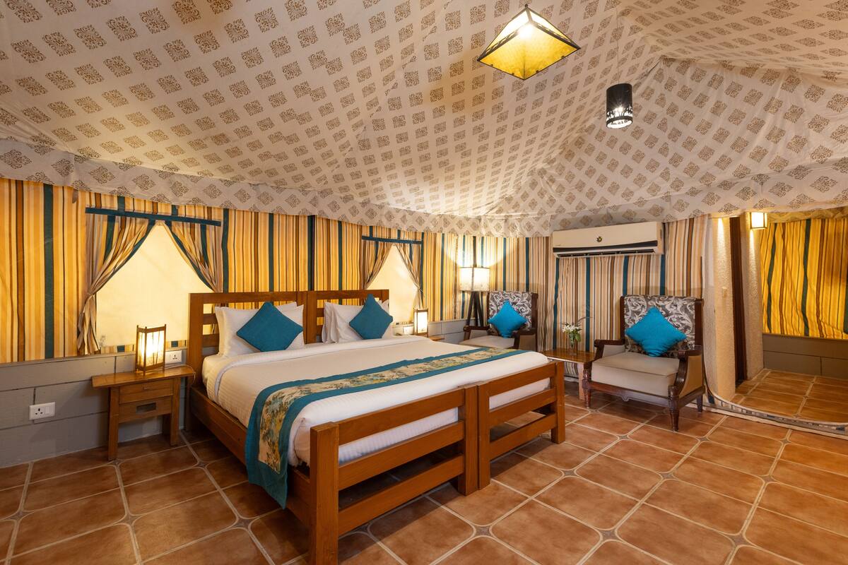 A bedroom with a large bed, a wooden chair, a nightstand, a lamp, and a ceiling light fixture.