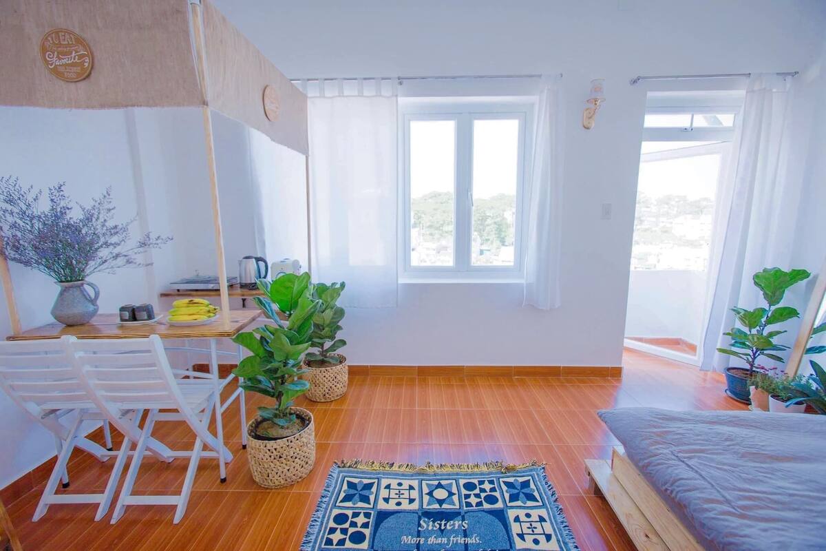 A bright room with a bed, a desk with a chair, and several potted plants.