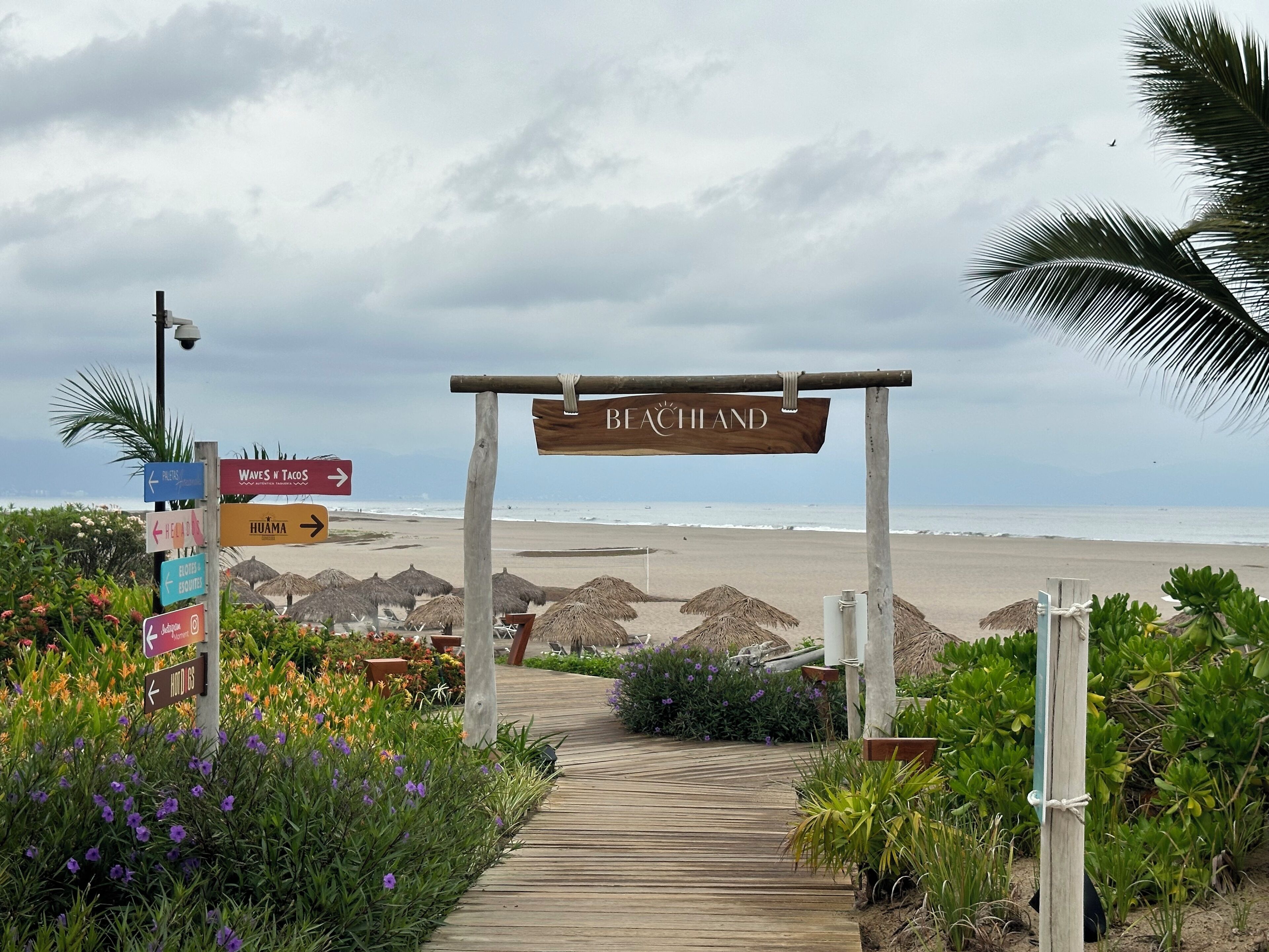 Un sendero de madera que conduce a una zona de playa con indicaciones y un cartel que dice 'BEACHLAND'.