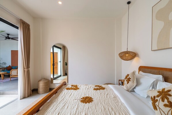 Un dormitorio con una cama grande, un ventilador de techo, una lámpara de fibras naturales y vista al área de estar.
