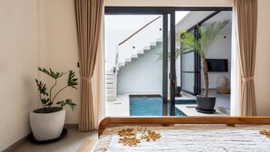 A bedroom with a large bed, a potted plant, and a view of a swimming pool and staircase. - Enaya Villa by Betterplace (Canggu)