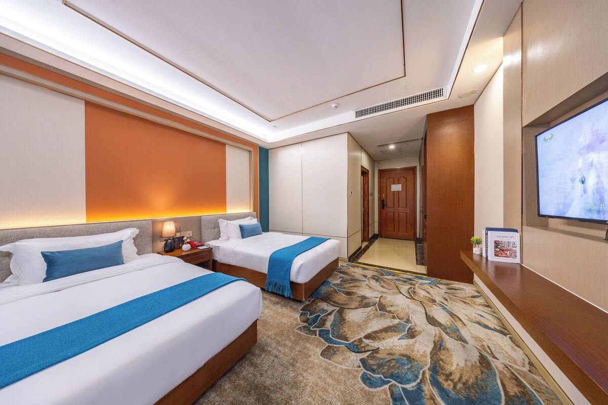 Habitación de hotel con dos camas, televisión, escritorio y piso alfombrado.