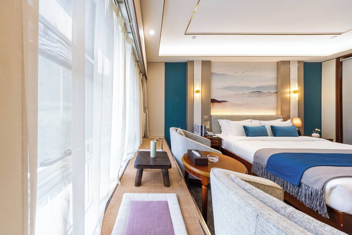 Habitación de hotel con una cama grande, un sofá, una mesita y vistas al exterior.