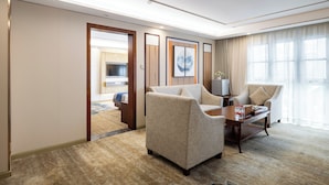 A hotel room with a sofa, armchairs, a coffee table, and a TV. There is a door leading to a bathroom and a hallway. - Xinrun Hua Hotel Hongqiao Park Branch (Shenzhen)