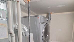 Une petite buanderie équipée d’un lave-linge et d’un sèche-linge, de tuyaux en métal et d’un coffret électrique.