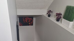 Un escalier avec une rampe en bois, un mur blanc et une petite étagère avec des plantes en pot.