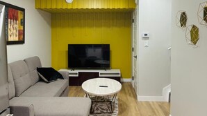 Un salon moderne avec un canapé, une table basse, un téléviseur à écran plat et un mur d’accent jaune.