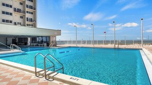 A swimming pool with clear blue water, a lifeguard stand, and a view of the ocean.