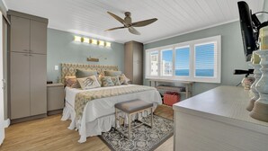 A bedroom with a bed, bedside tables, a desk, a chair, a wardrobe, a ceiling fan, and a window with blinds.
